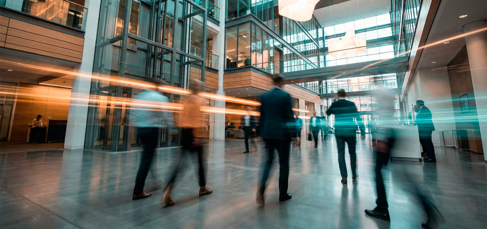 Dynamische Langzeitaufnahme einer modernen, belebten Büro-Empfangshalle mit Lichtspuren von Menschen, die ein agiles und modernes Arbeitsumfeld symbolisiert.